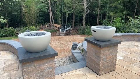 Outdoor stone steps leading to a patio with two large white planters on brick pillars, wooded backdrop