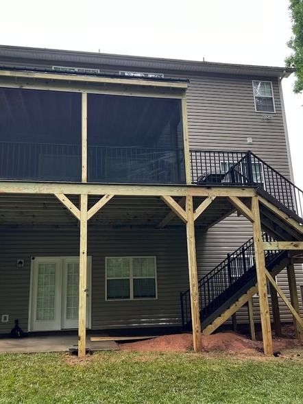 Two-story house exterior with screened upper porch, covered lower patio, and black metal staircase