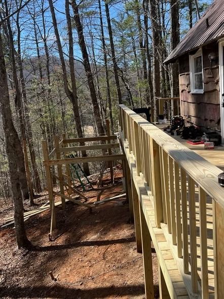 Wooden deck railing beside a house overlooking a wooded slope in winter.