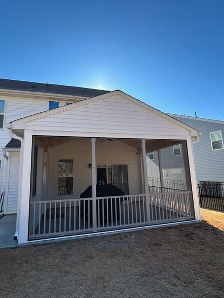 Covered white porch with railings attached to a house under a clear blue sky