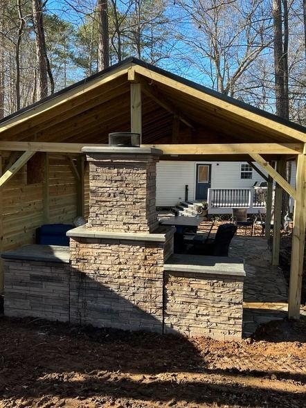 Wooden pavilion with stone fireplace and seating in a wooded yard