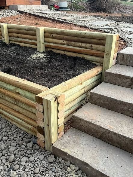 Timber raised garden bed beside concrete steps and gravel in a landscaped yard