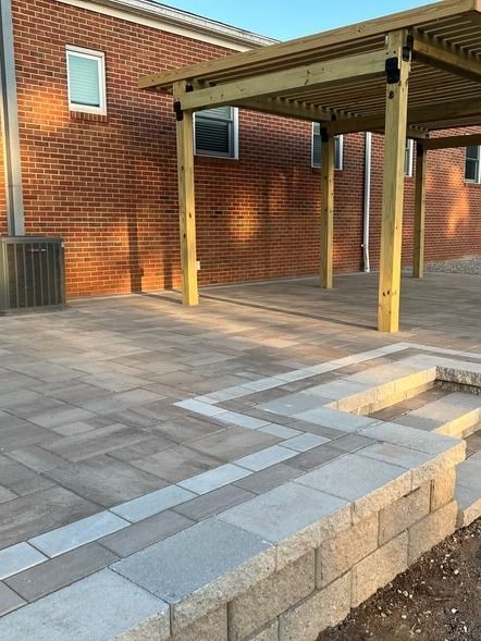 Brick courtyard with gray pavers, a raised stone step, and a covered wooden patio beside a brick building