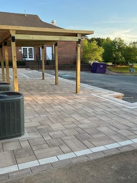 Brick patio beside a building with wooden posts, trash can, and a purple dumpster in the background