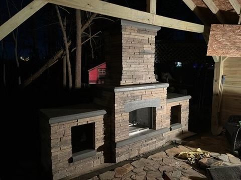 Outdoor brick fireplace and built-in grill under a roofed patio at night