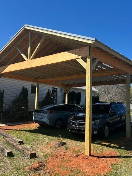Two cars parked under a wooden carport beside a house