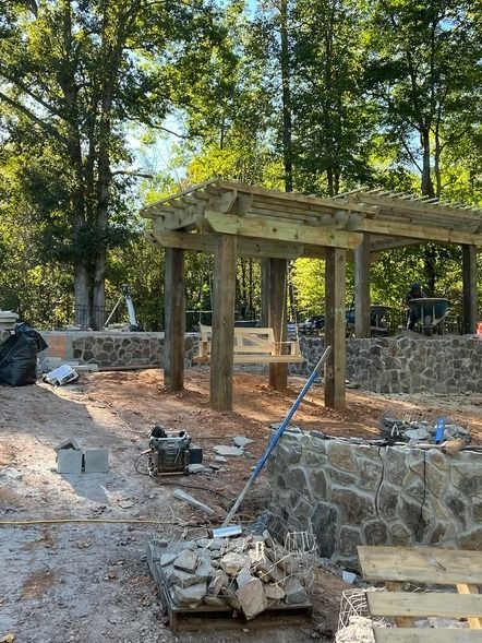 Wooden pergola under construction on a stone terrace in a wooded outdoor area