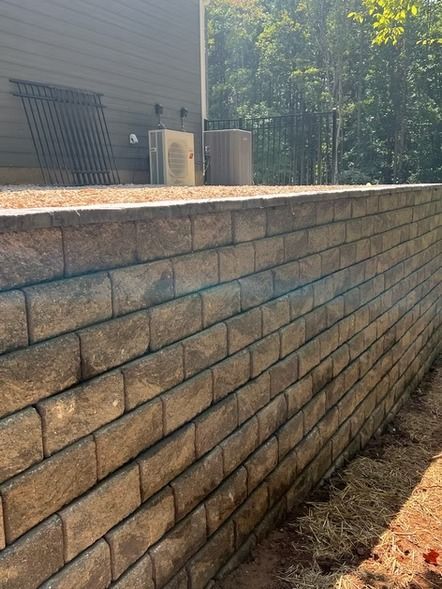Stone retaining wall beside a house, with sunlight and trees in the background