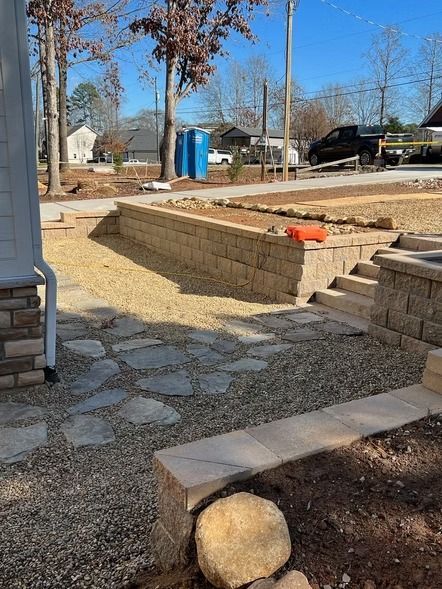 Backyard with stone steps, retaining walls, gravel path, and blue portable toilet in the distance