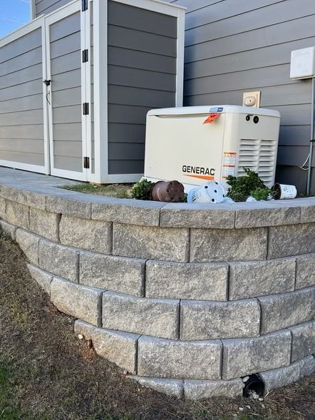 Generator beside a gray house on a curved stone retaining wall