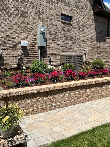 Brick house wall with red flowers in a raised bed beside a tiled walkway
