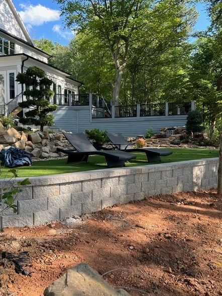 Backyard patio with stone wall, lounge chairs, and trees beside a house