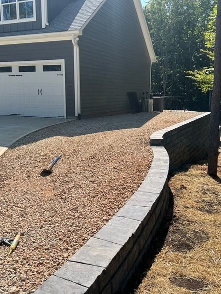 Curved stone retaining wall beside a gravel driveway and a house garage in daylight