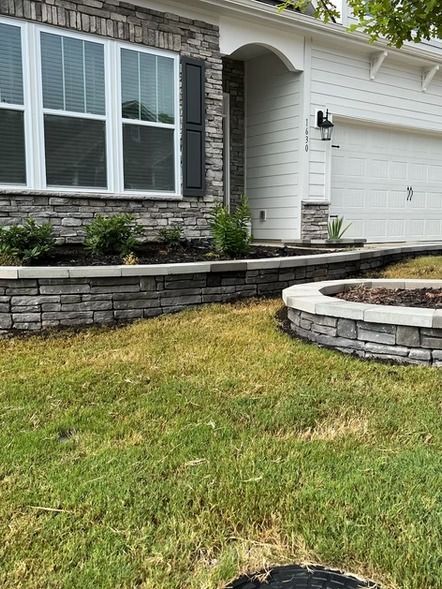 Front yard of a house with stone retaining walls, a lawn, and a small circular raised garden bed.