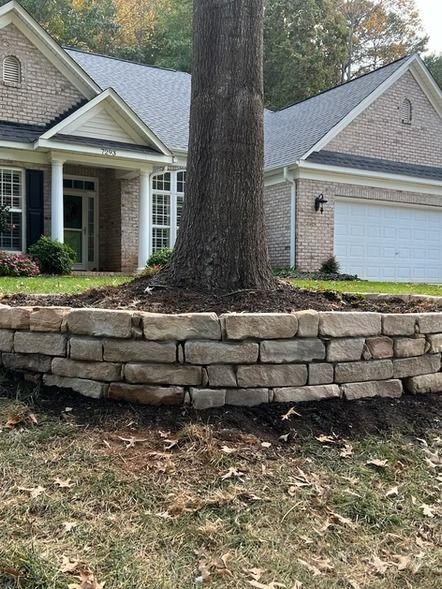 Stone retaining wall around large tree in front yard of a suburban house with garage