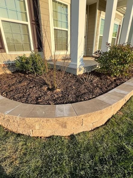 Front yard garden bed with mulch, shrubs, and stone edging beneath house windows and columns