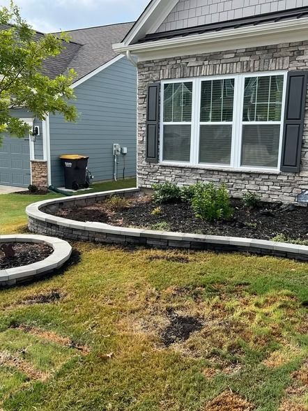 Suburban house front yard with curved stone border, patchy grass, and large windows with dark shutters
