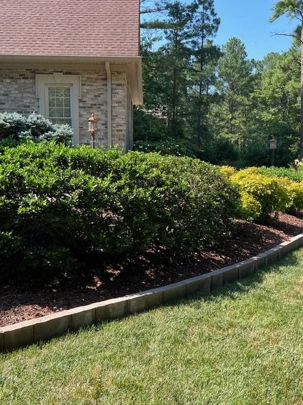 Landscaped front yard with trimmed shrubs, grass, and a brick house corner in sunlight
