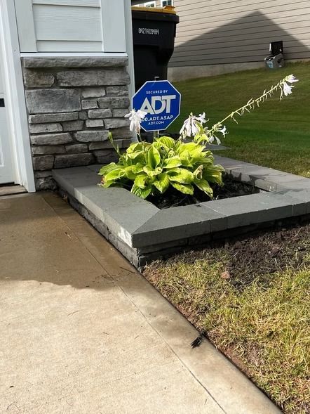Front yard flower bed with an ADT security sign beside a house and sidewalk