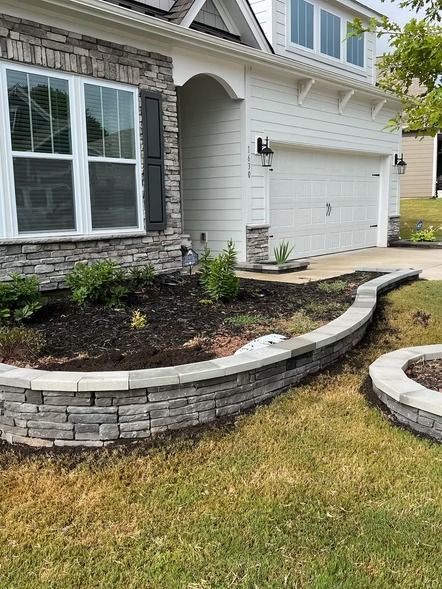 Front yard with curved stone retaining wall, mulch bed, and white house exterior with garage and windows