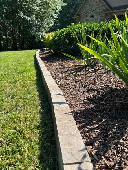 Curved stone garden edging beside a mulched flower bed and green lawn in sunlight