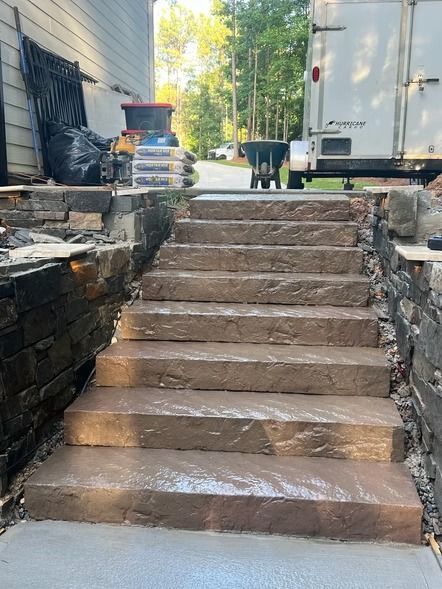 Stone steps leading up a sloped outdoor driveway between retaining walls, with a truck and bins at the top.