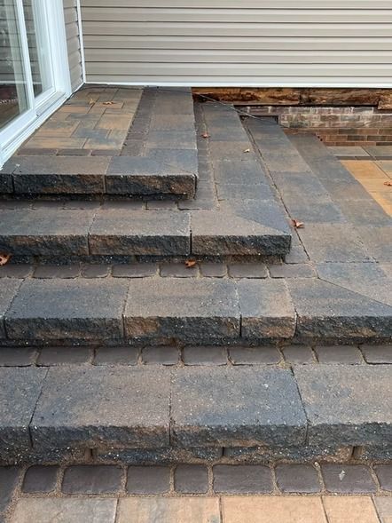 Tiered stone patio steps with dark pavers and a sliding glass door on the left