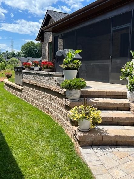 Front steps of a house with tiered stone retaining wall and potted plants along a sunny walkway