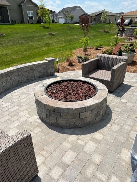 Back patio with a circular stone fire pit, wicker chairs, and a landscaped backyard beyond.