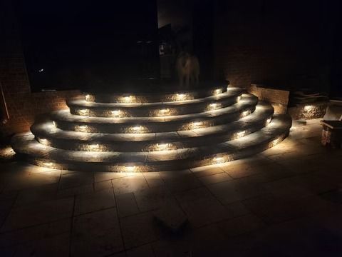 Curved stone steps lit by warm lights at night in a dark outdoor plaza