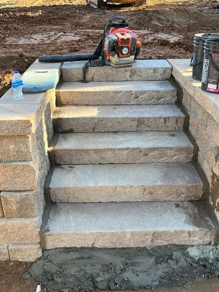 Stone steps under construction with a chainsaw and tools on top, and wet concrete at the base.