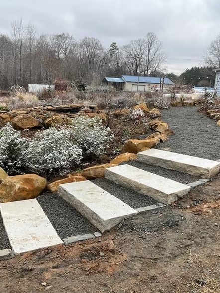 Stepping stones across a gravel garden path beside a landscaped rock bed and bare trees