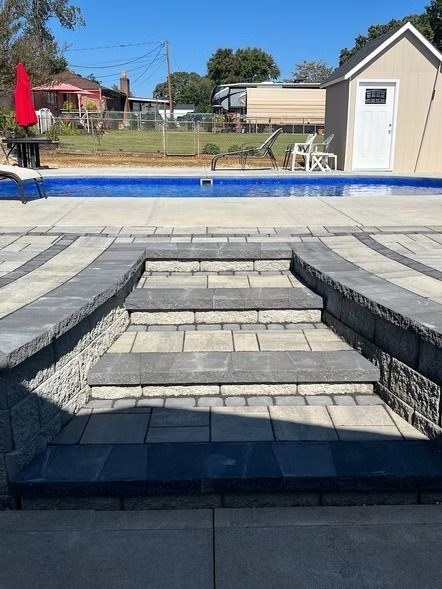 Poolside stone steps leading to a raised deck, with a blue pool and white shed in the background.