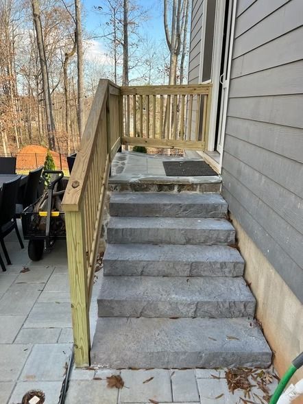 Outdoor stone staircase with wooden railing leading to a small deck beside a house
