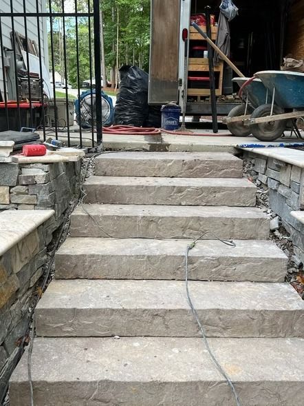 Stone steps leading to a backyard deck, with wheelbarrow, tools, and construction materials on either side