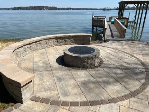 Stone fire pit on a circular patio by a calm waterfront dock on a sunny day