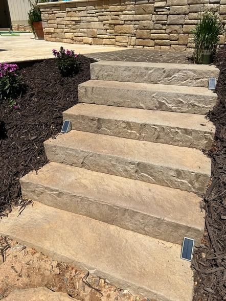 Stone outdoor steps with small blue lights leading up to a patio against a stone wall