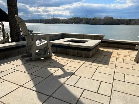 Patio with stone fire pit, chair, and river view under a cloudy sky