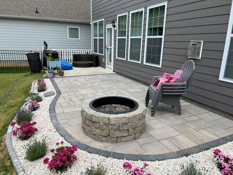 Backyard patio with stone fire pit, pink flowers, and lounge chairs beside a house