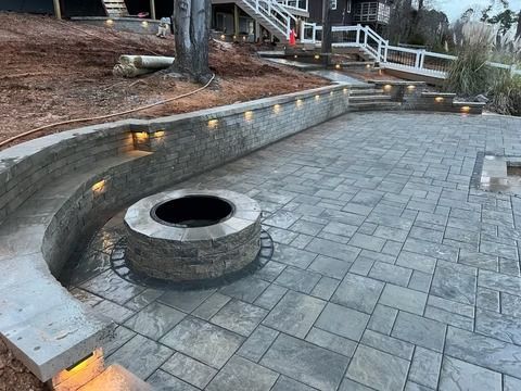 Stone patio with curved retaining wall, built-in lights, and a circular fire pit near steps and trees