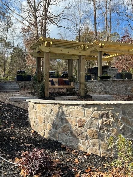 Stone pergola in a wooded park with a circular retaining wall and picnic tables