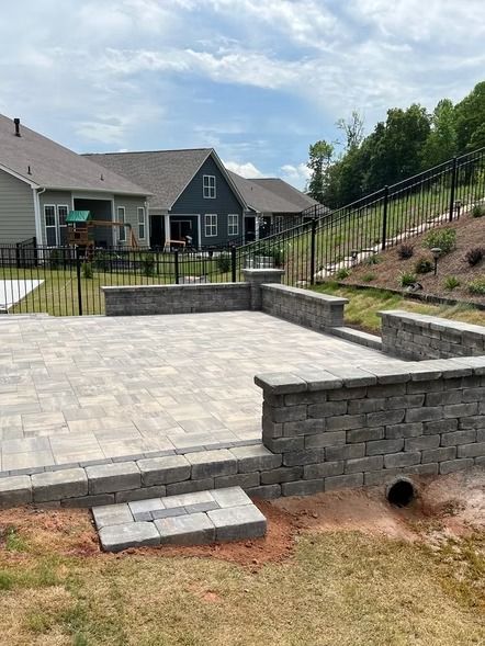 Backyard paver patio with stone retaining walls, stairs, and a grassy slope behind a house