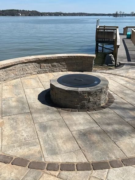 Stone fire pit on a waterfront patio with calm water and a small dock in the background