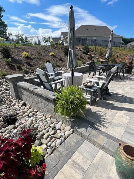 Patio with gray stone pavers, fire pit seating, closed umbrella, and landscaped gravel garden under blue sky