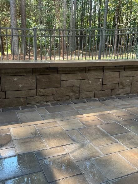 Stone patio with a low retaining wall and black metal fence in a wooded park setting