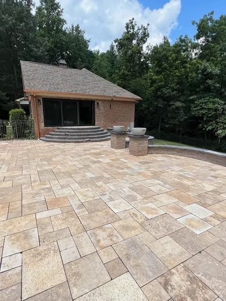 Stone patio with brick house and trees under a partly cloudy sky