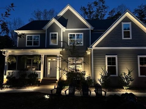 Two-story suburban house at night, warmly lit windows and porch lights, with trees and dark blue sky.
