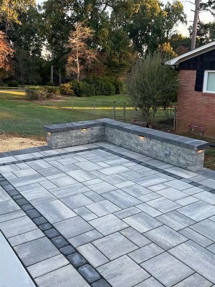 Gray stone patio with built-in bench beside a brick house and grassy yard at sunset