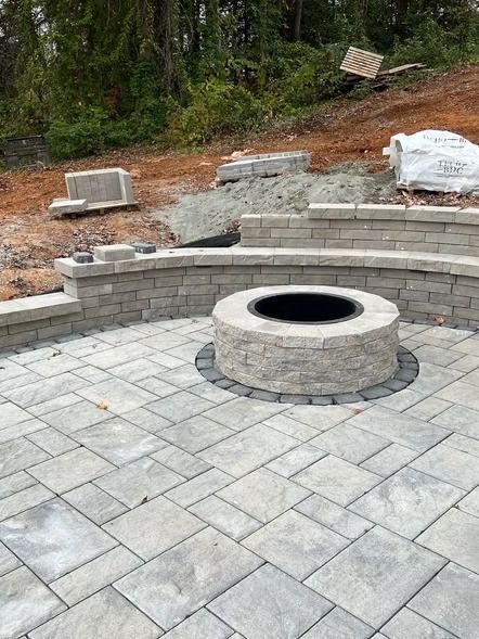 Stone patio with a circular fire pit and curved retaining wall in a landscaped backyard