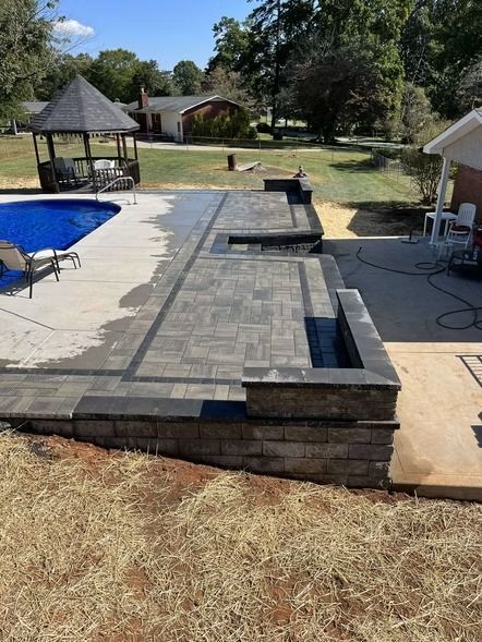 Backyard patio with raised stone pool deck, blue swimming pool, and gazebo under construction